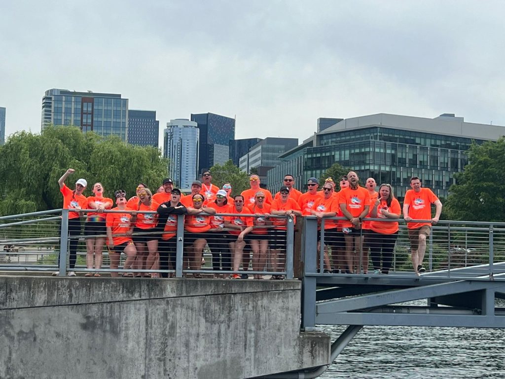 Crew cheering from a bridge over the water, Seattle skyline behind